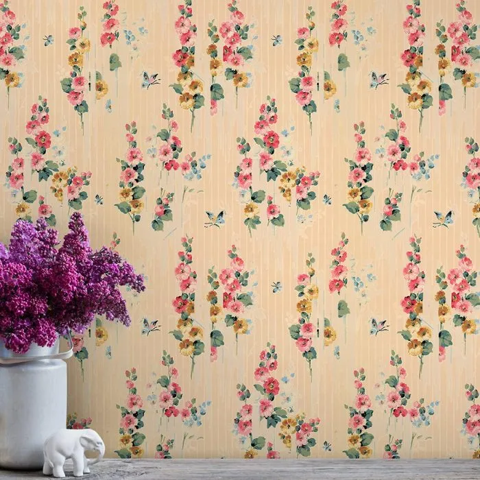 The Hollyhock wallpaper, in beige with vintage vertical stripes and pink, yellow, and green floral patterns, adds charm to this set featuring a white vase with purple flowers and a white elephant figurine on a wooden surface.
